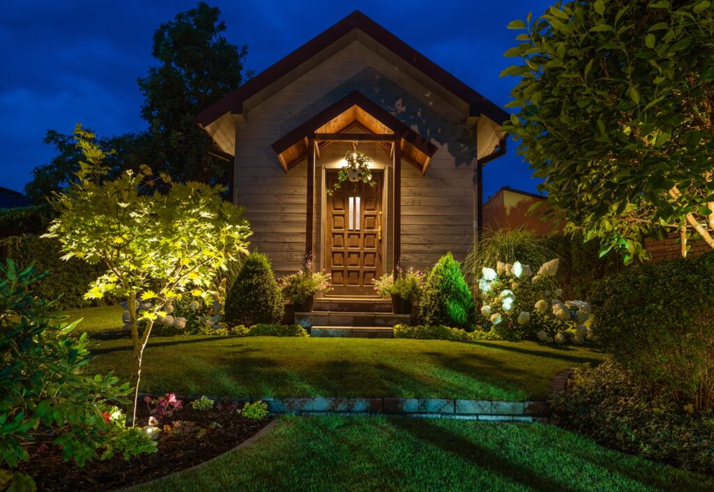 outdoor lighting - example of uplighting - ambient lights are shining at decorative trees and bushes at night near a backyard bonus shed