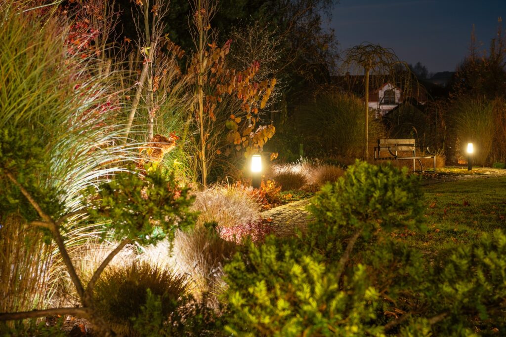 garden path is illuminated by soft lights, surrounded by autumn foliage and a cozy bench under the evening sky, creating a serene atmosphere.