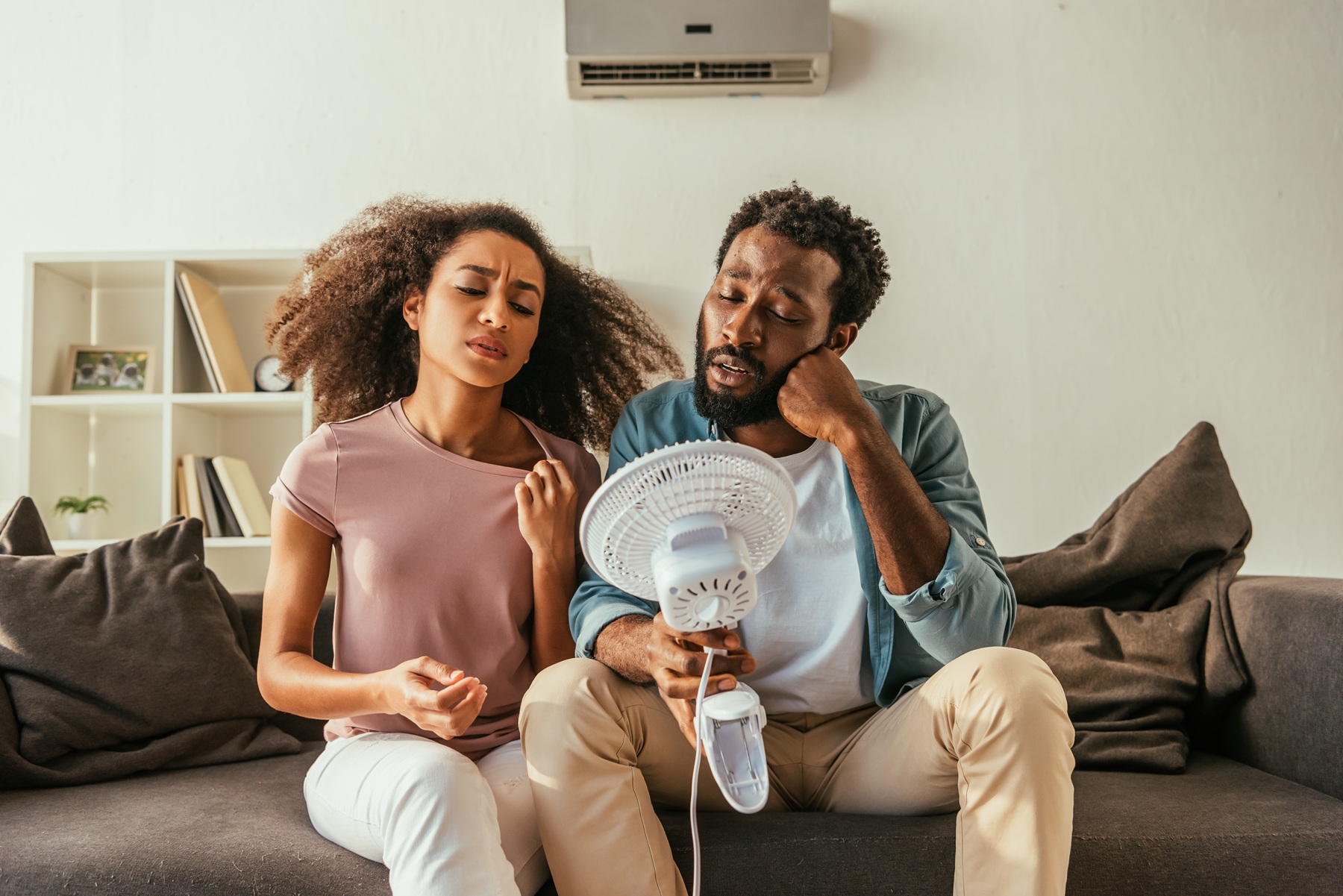 african american couple with broken AC holding fan in very hot house